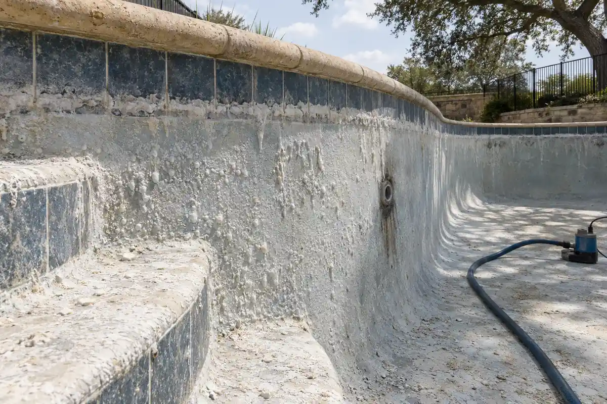 White calcium scale and volcano-shaped nodules on a drained pool wall below a crusted waterline tile band