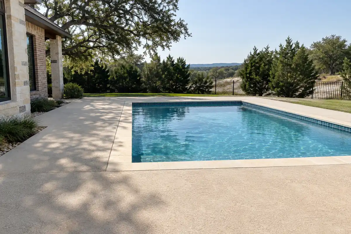 Finished light-colored concrete pool deck meeting limestone coping around a full pool under a live oak canopy