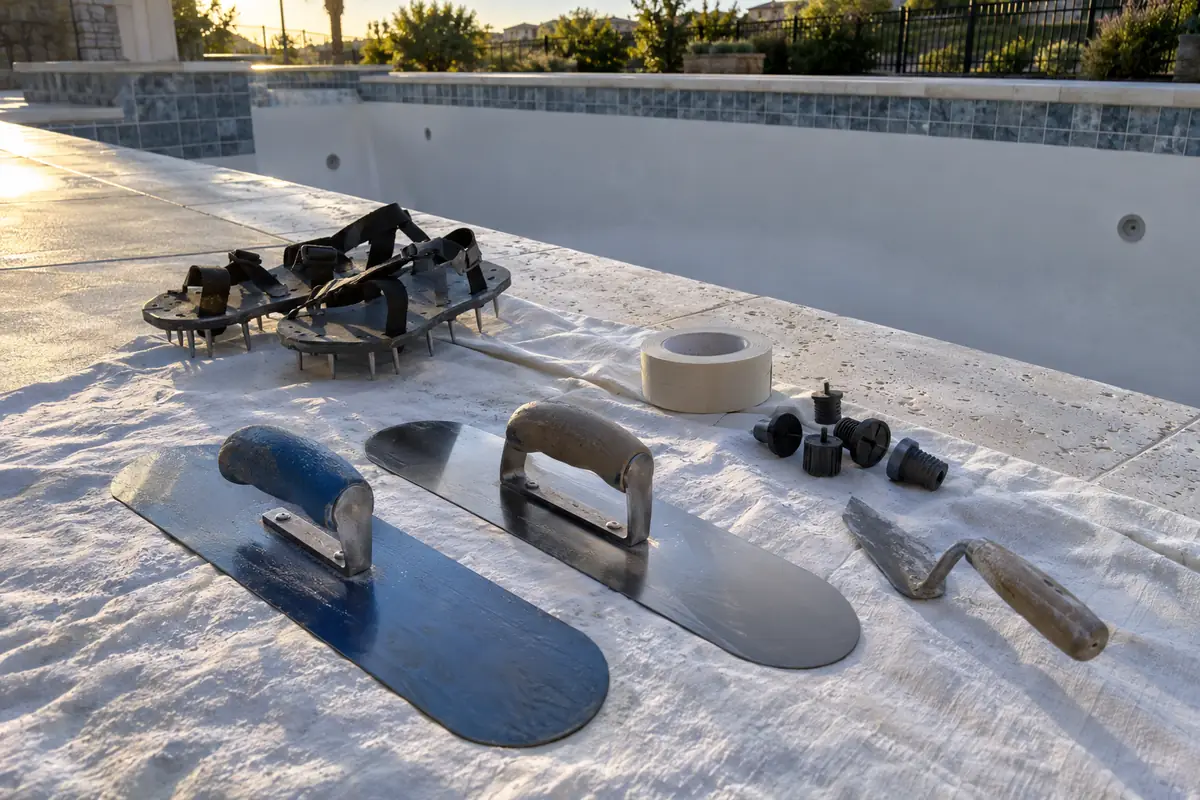 Pool trowels with rounded ends and spiked shoes laid on a sheet at the coping after plaster day